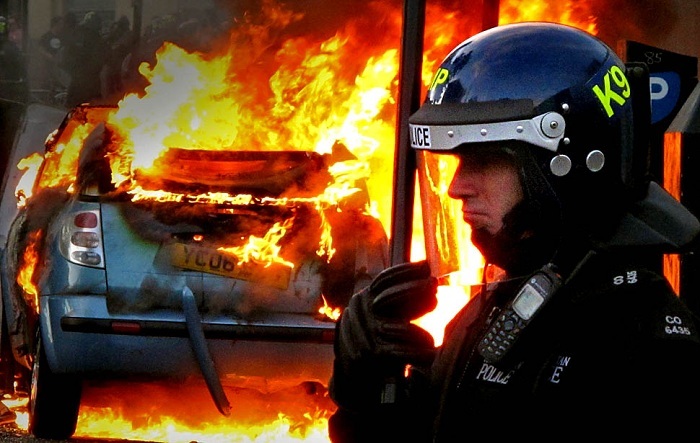 brytyjski-policjant-na-tle-palacego-sie-samochodu-podczas-zamieszek-w-londynie-sierpien-2011.jpg